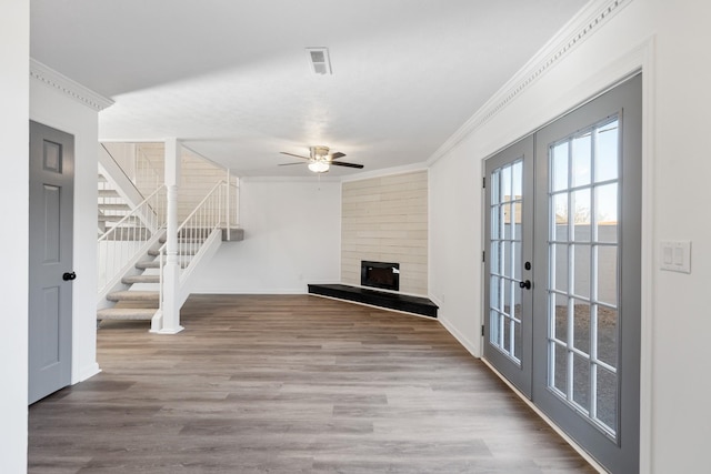 unfurnished living room featuring wood-type flooring, a large fireplace, crown molding, and french doors