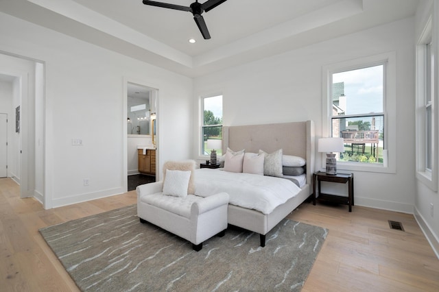 bedroom with ceiling fan, ensuite bathroom, a raised ceiling, and light wood-type flooring