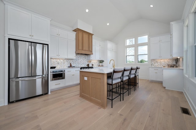 kitchen with vaulted ceiling, appliances with stainless steel finishes, white cabinetry, a kitchen bar, and a kitchen island with sink