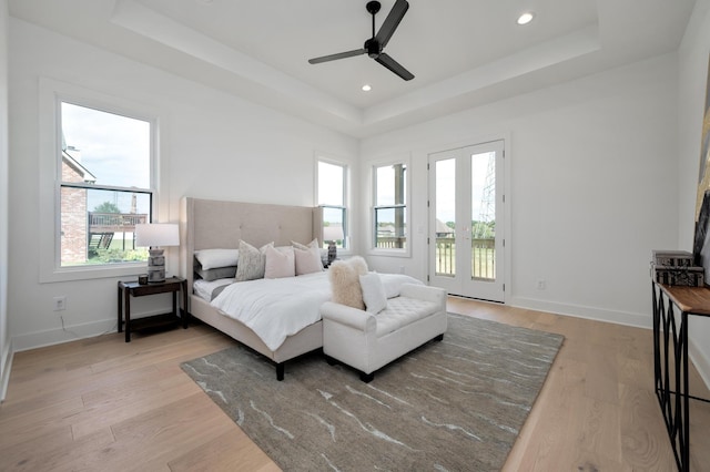 bedroom with ceiling fan, a tray ceiling, light wood-type flooring, and access to outside