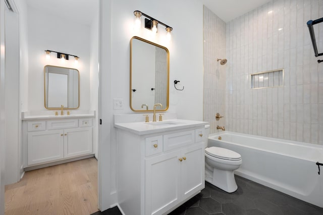 full bathroom with hardwood / wood-style flooring, tiled shower / bath, vanity, and toilet