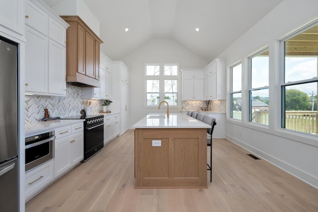 kitchen with sink, white cabinetry, vaulted ceiling, stainless steel appliances, and a kitchen island with sink