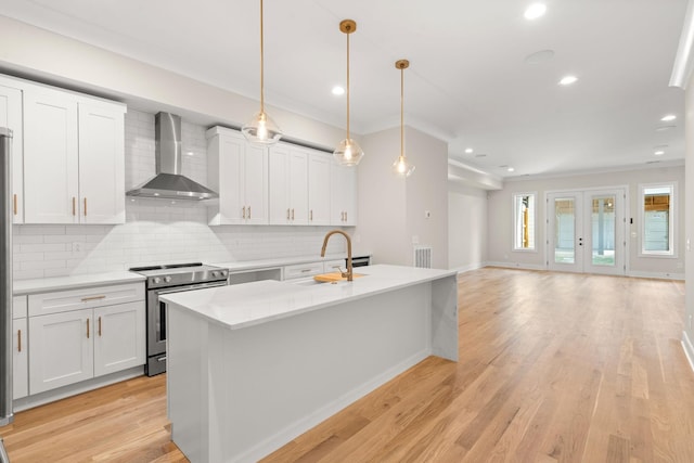 kitchen with wall chimney exhaust hood, decorative light fixtures, an island with sink, stainless steel electric stove, and white cabinets