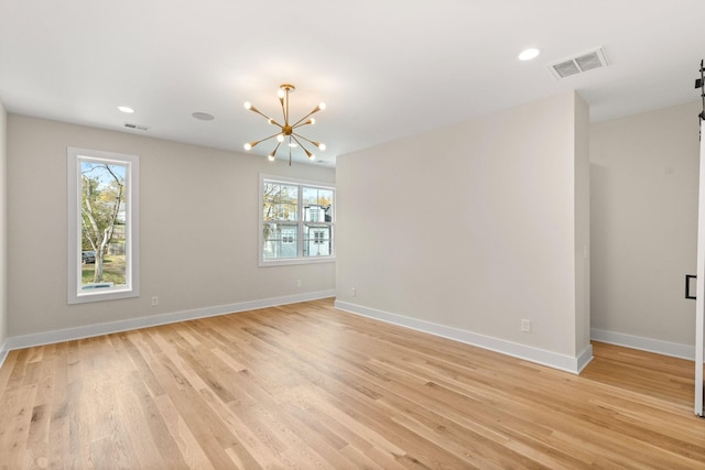 unfurnished room with a barn door, a chandelier, and light wood-type flooring