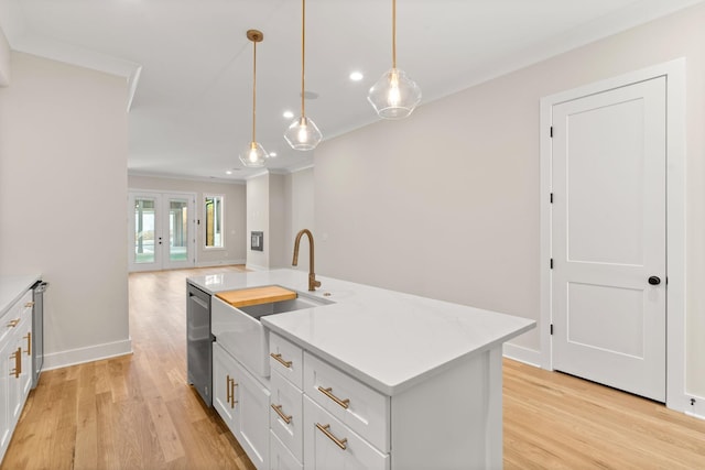 kitchen featuring light stone counters, decorative light fixtures, light wood-type flooring, an island with sink, and white cabinets