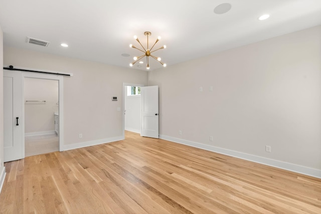 unfurnished room featuring a notable chandelier, light hardwood / wood-style flooring, and a barn door