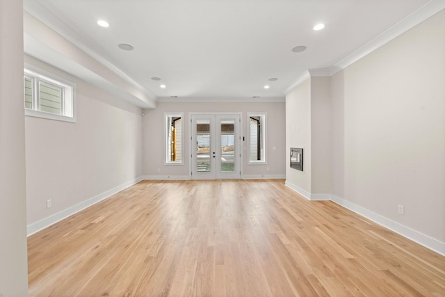 unfurnished living room with crown molding, a wealth of natural light, french doors, and light wood-type flooring