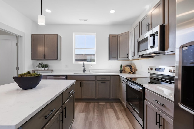 kitchen with sink, decorative light fixtures, appliances with stainless steel finishes, hardwood / wood-style flooring, and light stone countertops