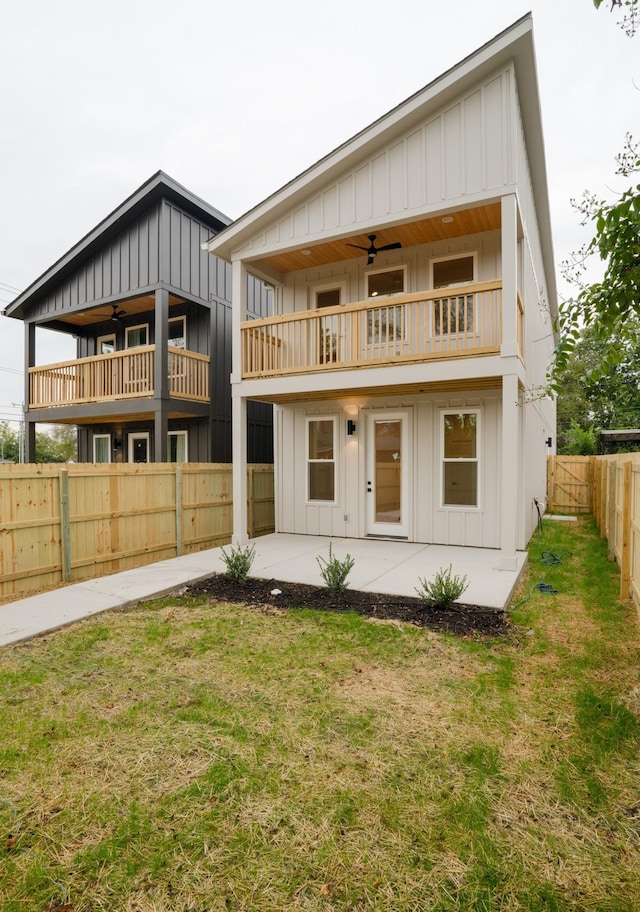 rear view of house with ceiling fan, a balcony, a patio area, and a lawn