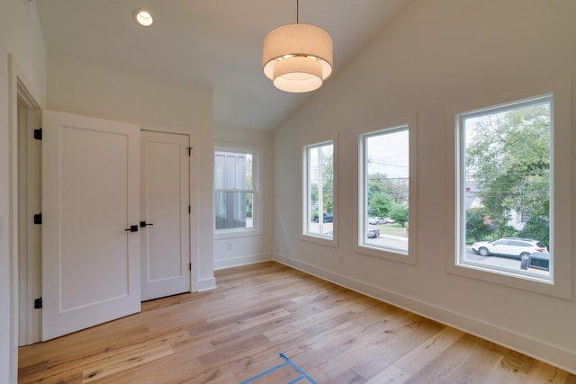 unfurnished bedroom featuring multiple windows, lofted ceiling, and light wood-type flooring