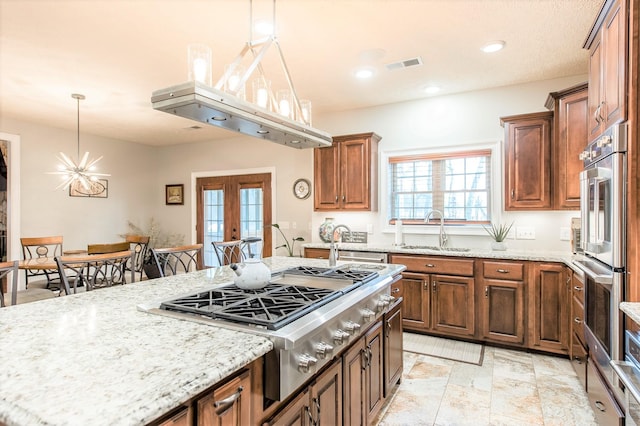 kitchen featuring pendant lighting, sink, appliances with stainless steel finishes, light stone countertops, and french doors