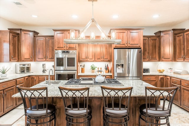 kitchen featuring pendant lighting, a breakfast bar area, stainless steel appliances, light stone countertops, and a center island with sink