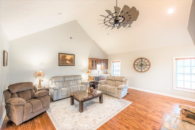 living room with ceiling fan, beverage cooler, high vaulted ceiling, and light hardwood / wood-style flooring