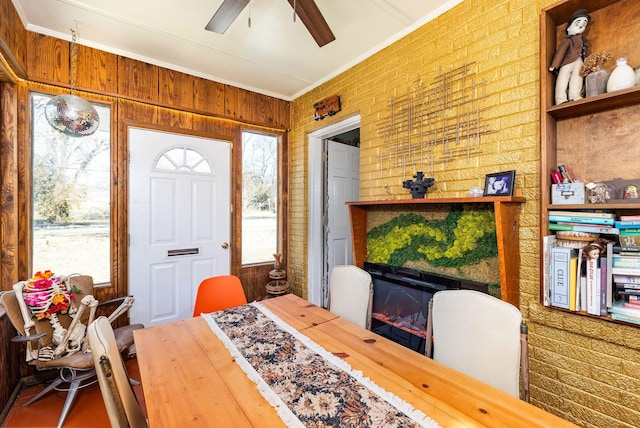 dining room featuring ornamental molding, brick wall, ceiling fan, and a fireplace