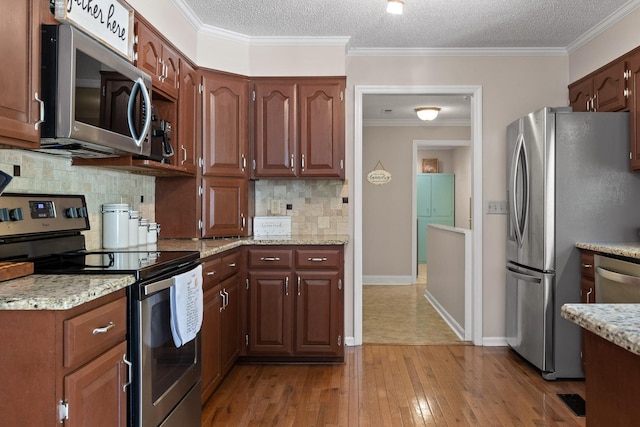 kitchen featuring light wood-type flooring, ornamental molding, stainless steel appliances, light stone countertops, and decorative backsplash