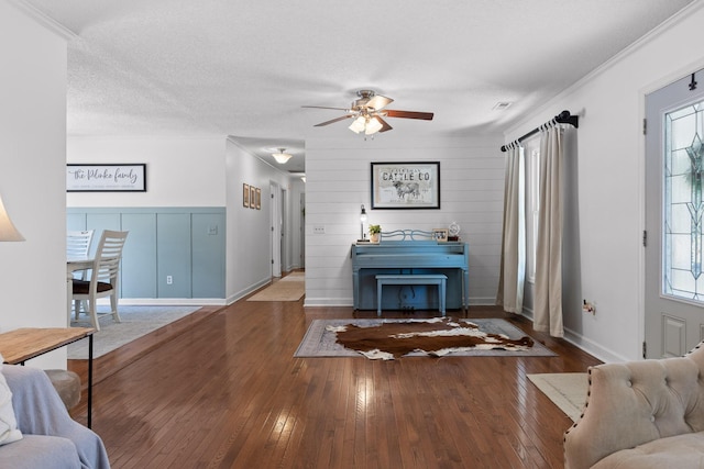 living room featuring ceiling fan, dark wood-type flooring, ornamental molding, and a textured ceiling