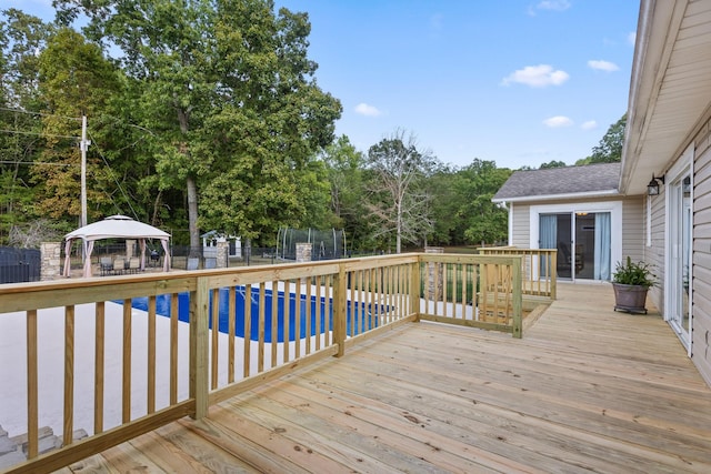 wooden terrace featuring a pool, a gazebo, and a trampoline