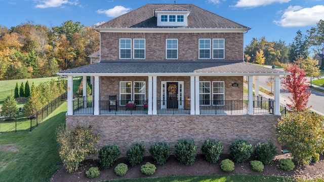 view of front facade featuring a porch, brick siding, a front lawn, and roof with shingles