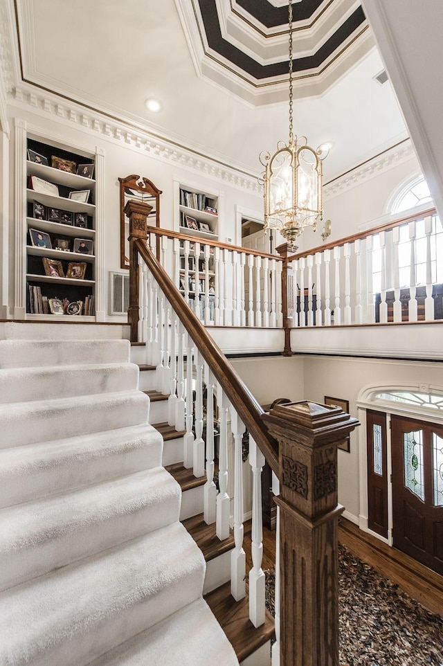 stairway with crown molding, a notable chandelier, a tray ceiling, wood-type flooring, and built in shelves