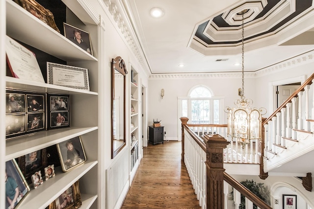 hall featuring hardwood / wood-style floors, built in features, ornamental molding, and a chandelier