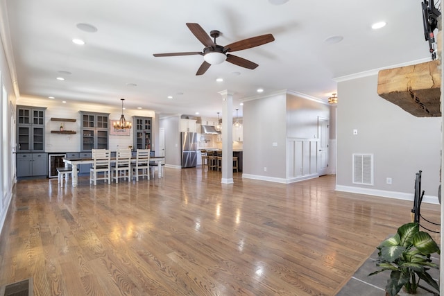 living room featuring hardwood / wood-style floors, wine cooler, ornamental molding, ceiling fan with notable chandelier, and ornate columns