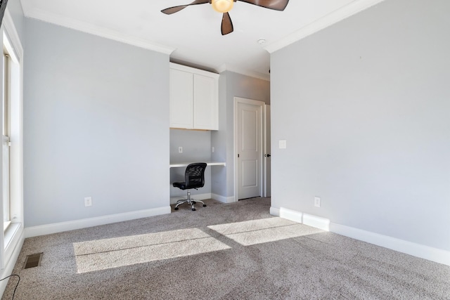 unfurnished bedroom featuring ornamental molding, built in desk, light colored carpet, and ceiling fan