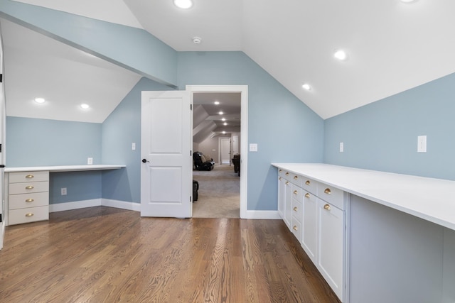 interior space with white cabinetry, built in desk, dark hardwood / wood-style floors, and vaulted ceiling