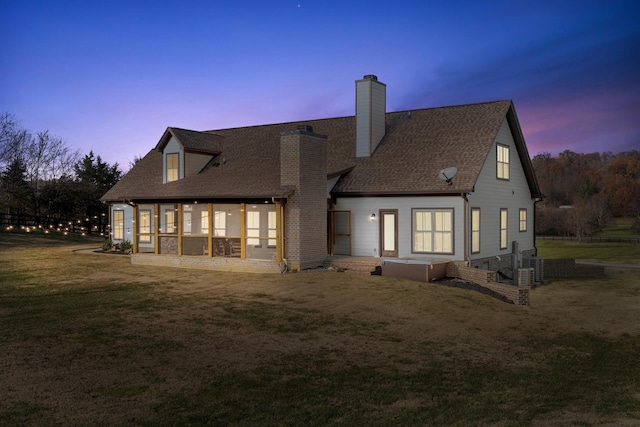 back house at dusk featuring central AC unit, a sunroom, and a lawn