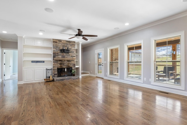 unfurnished living room with ceiling fan, hardwood / wood-style floors, a fireplace, ornamental molding, and built in shelves