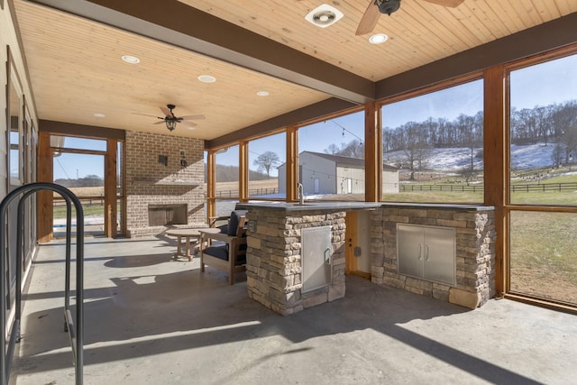 unfurnished sunroom featuring wood ceiling, plenty of natural light, a large fireplace, and ceiling fan