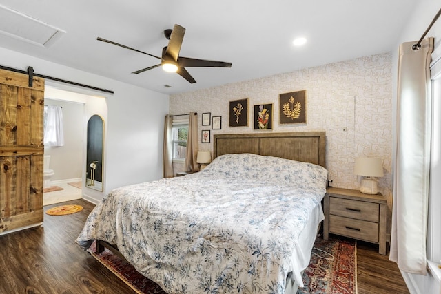 bedroom featuring ensuite bathroom, a barn door, dark wood-type flooring, and ceiling fan