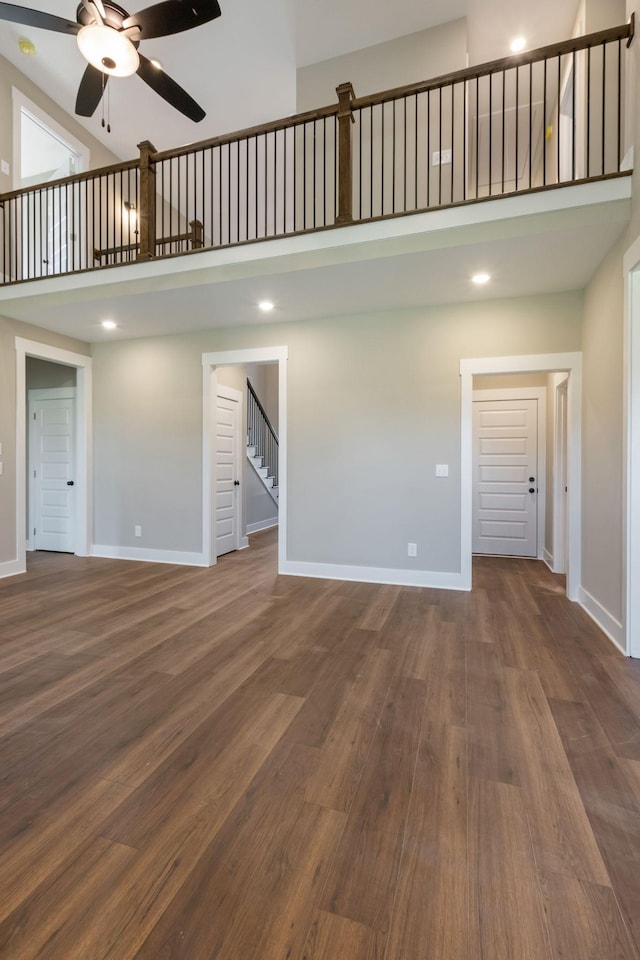 unfurnished living room featuring stairs, a towering ceiling, baseboards, and ceiling fan
