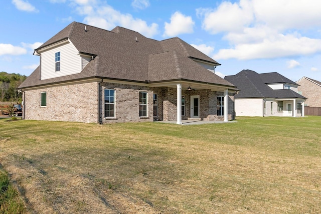 back of house featuring a patio, a shingled roof, a lawn, and brick siding