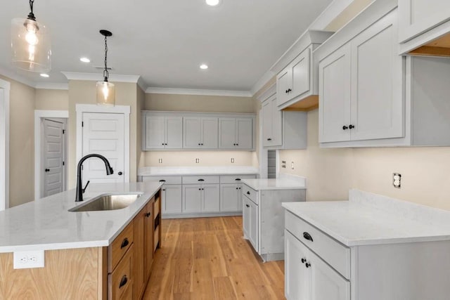 kitchen featuring light wood-type flooring, an island with sink, a sink, and ornamental molding