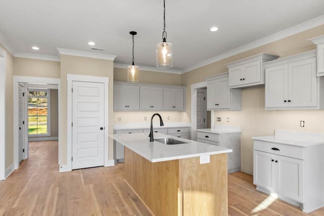 kitchen featuring ornamental molding, visible vents, a kitchen island with sink, a sink, and light wood finished floors