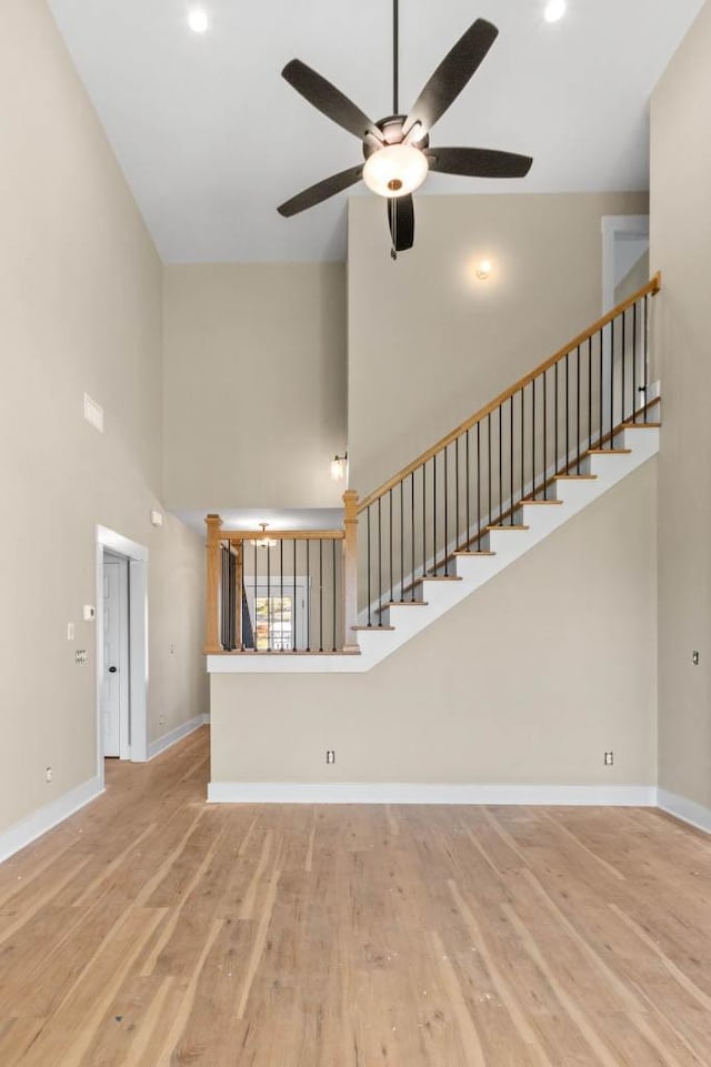 unfurnished living room with stairway, a ceiling fan, wood finished floors, and a towering ceiling