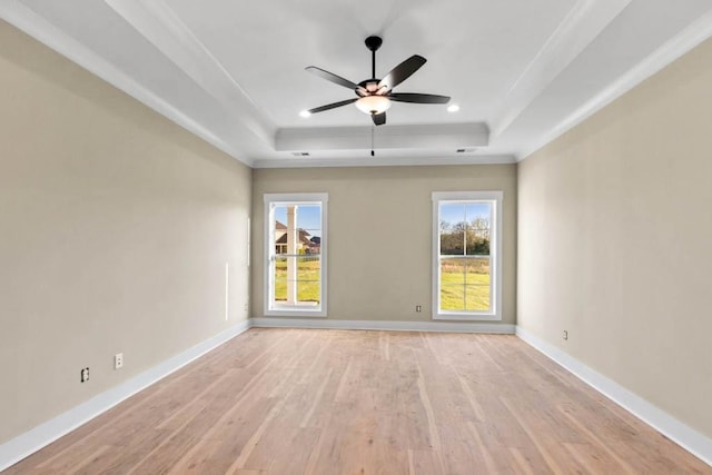 empty room with a tray ceiling, baseboards, and light wood finished floors
