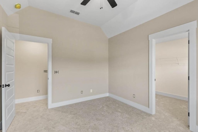 empty room with baseboards, vaulted ceiling, a ceiling fan, visible vents, and light colored carpet