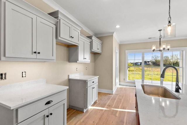 kitchen featuring baseboards, light stone counters, decorative light fixtures, light wood finished floors, and a sink