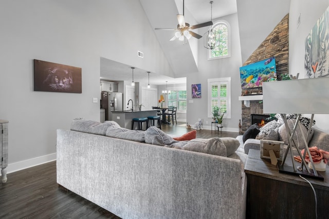 living room with a stone fireplace, a wealth of natural light, high vaulted ceiling, and ceiling fan with notable chandelier