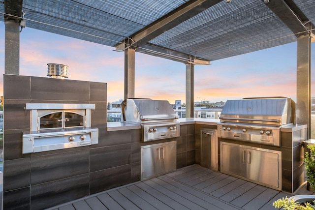 deck at dusk with a pergola, grilling area, and exterior kitchen