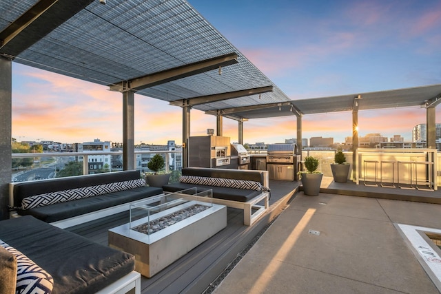 deck at dusk featuring an outdoor kitchen, an outdoor living space with a fire pit, and grilling area