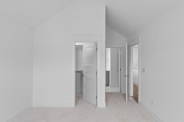 unfurnished bedroom featuring lofted ceiling, a walk in closet, and light carpet