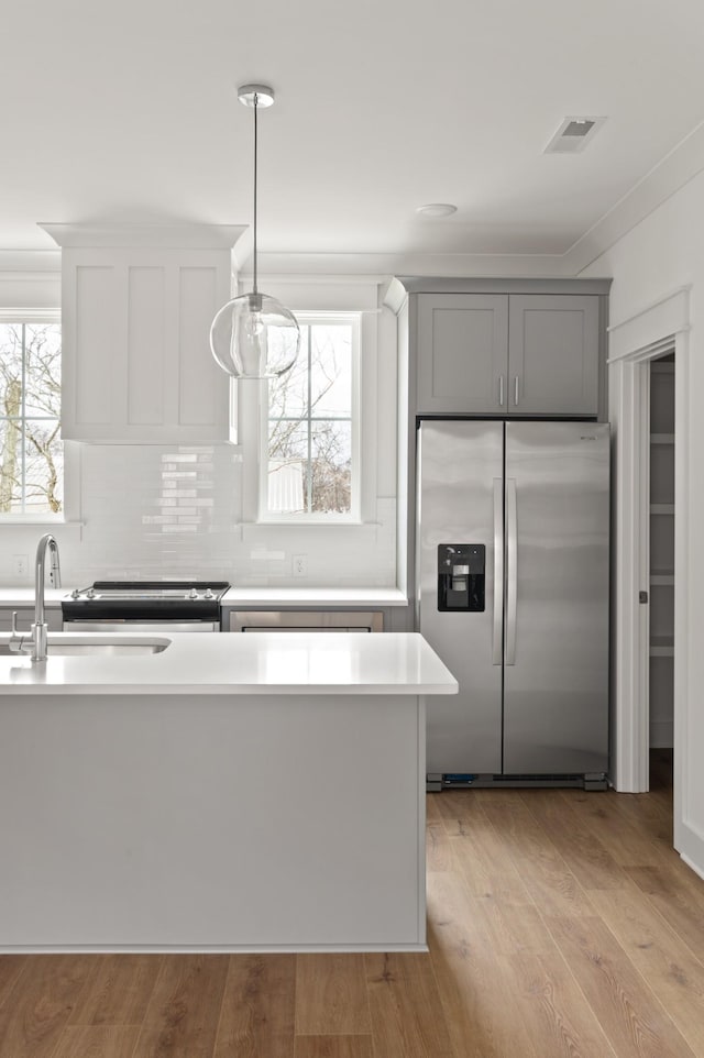 kitchen with stainless steel refrigerator with ice dispenser, sink, gray cabinets, pendant lighting, and light hardwood / wood-style floors