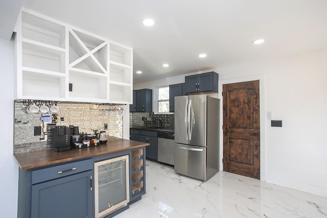 kitchen featuring blue cabinetry, wooden counters, appliances with stainless steel finishes, beverage cooler, and decorative backsplash