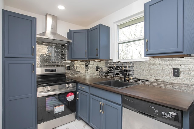 kitchen with wood counters, wall chimney exhaust hood, blue cabinets, sink, and stainless steel appliances