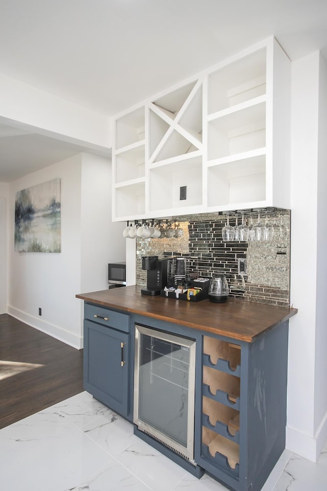 bar featuring tasteful backsplash, blue cabinets, beverage cooler, and butcher block counters