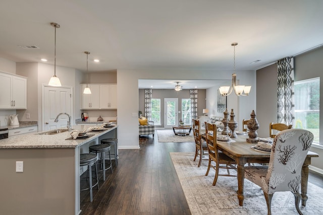 dining space with ceiling fan with notable chandelier, sink, and dark wood-type flooring