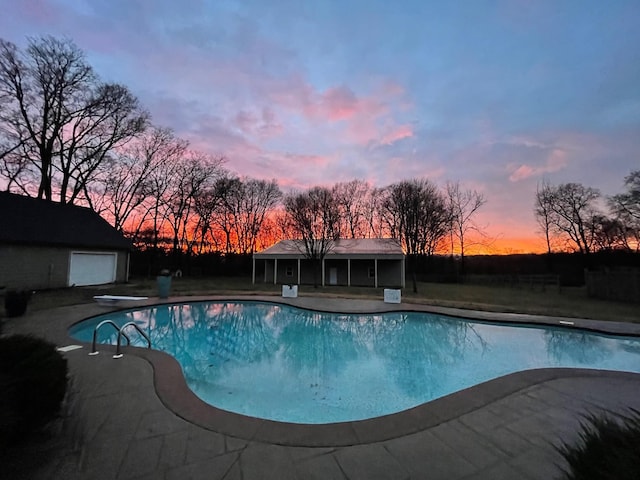 pool at dusk featuring a garage, an outdoor structure, and a diving board