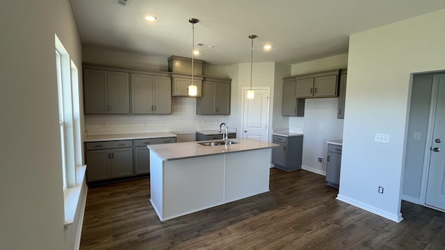 kitchen featuring sink, dark hardwood / wood-style floors, pendant lighting, a kitchen island with sink, and decorative backsplash